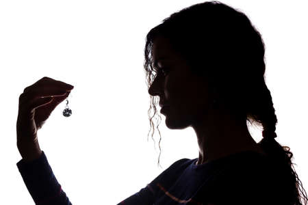 Young woman look ahead with flowing hair with an earring in his hand - isolated silhouetteの写真素材
