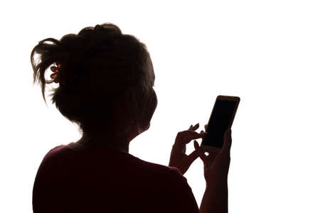 Silhouette of a girl from the back with a mobile smart phone - isolated, technologyの写真素材