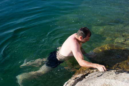 Young man, swimmer on the background of stones and water - feeling bad, swimming lessons, divingの写真素材