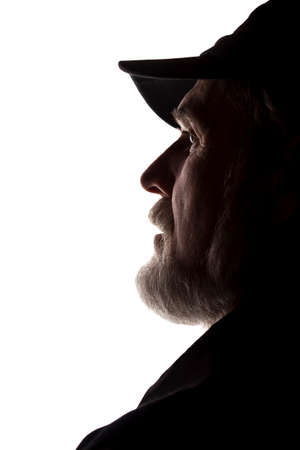 Portrait of a old man, in a peaked cap, with beard, side view - dark isolated silhouetteの写真素材