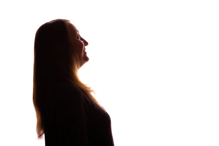Silhouette of a young woman with long, loose hair looking upwards with a thoughtful and pleading expression. Isolated on a white background. The image conveys emotions of hope, contemplation, vulnerability, and silent request. Minimalist studio shot ideal for symbolic, emotional, or inspirational visual content.の写真素材