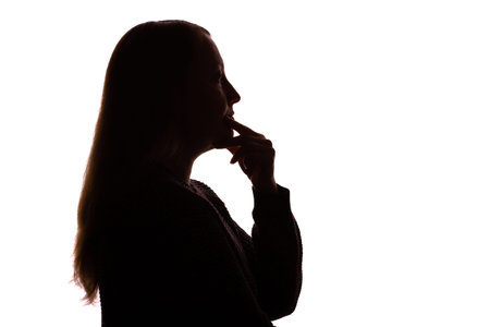 Silhouette of a young woman with long, loose hair, gently touching her chin in a thoughtful pose while looking forwards. Isolated on a white background. The image conveys introspection, subtle emotion, and quiet contemplation. Clean, minimalist studio composition suitable for symbolic, emotional, or inspirational visual projects.の写真素材