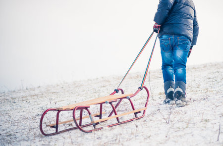 boy dragging sleds on snowy hill