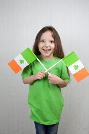Smiling cute girl in green clothes with flags of Ireland with clover leaves in her hands. Saint...
