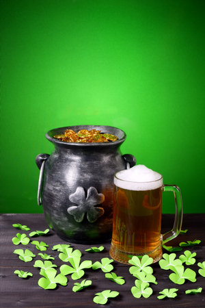 Cast iron pot with four-petal lucky shamrock leaf, mug of beer, clover leaves on dark wooden table...