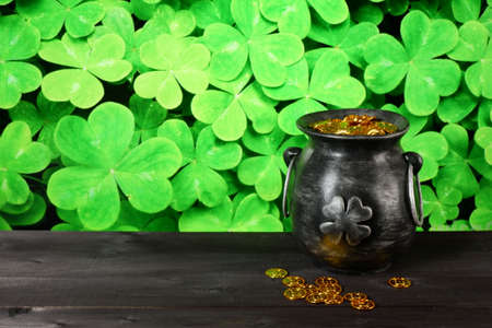Cast iron pot, decorated by four-petal lucky shamrock leaf, full of leprechaun gold treasure on wooden table, shamrock leaves backround. Saint Patricks Day banner, poster, flyer, invitation templateの写真素材