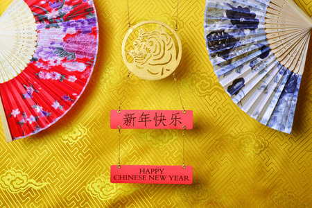 Gold tiger symbol and pair of chinese bamboo paper fans on yellow fabric with traditional chinese ornament with clouds. Chinese New Year of the Tiger 2022. Translation: happy new yearの写真素材