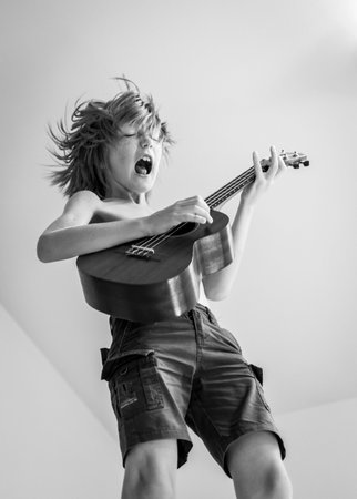 Young blond boy gets fun playing ukulele and jumpingの写真素材