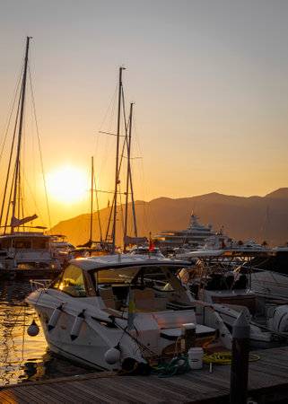 Serene Sunset Over a Tranquil Marina: Boats, Yachts, and Sailboats Reflect in Calm Waters Against a Majestic Mountain Backdrop.の写真素材