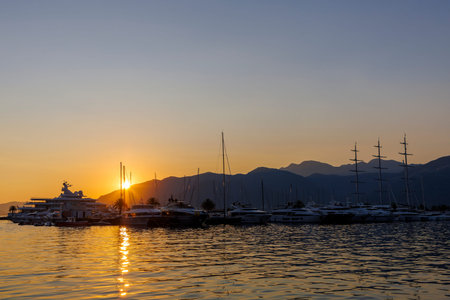 Serene Sunset Over a Tranquil Marina: Boats, Yachts, and Sailboats Reflect in Calm Waters Against a Majestic Mountain Backdrop.の写真素材