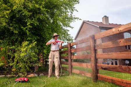A man is cleaning wooden fence with electric power washerの写真素材