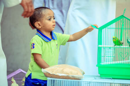 NIZWA, OMAN, MAY 27, 2016: an Omani boy is interesed in a parakeet at the bird market in Nizwa, Omanのeditorial素材