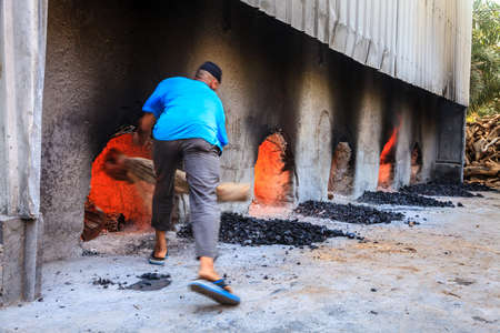 NIZWA, OMAN, MAY 27, 2016: Halwa factory worker is trowing log into a wood fired oven under halwa kettlesのeditorial素材