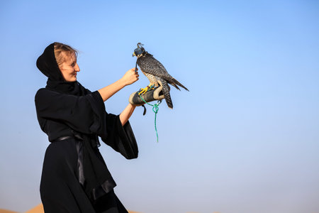Young woman in abaya with Peregrine Falcon in Dubai Desert Conservation Reserve, UAEの写真素材