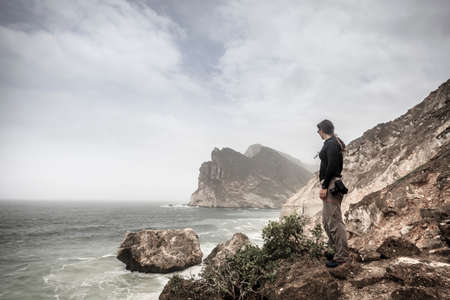 Woman photographer watching the sea from a cliff on Oman coastの写真素材