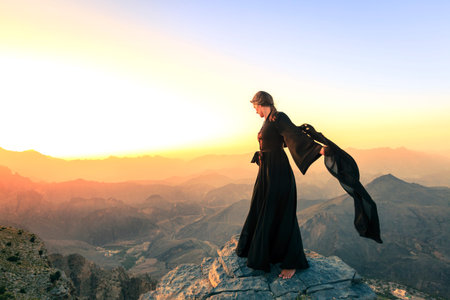Lone woman in abaya in Al Hajar Mountains of Oman at sunset