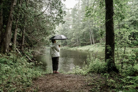 Woman with umbrella standing on a river bank in the rainの写真素材