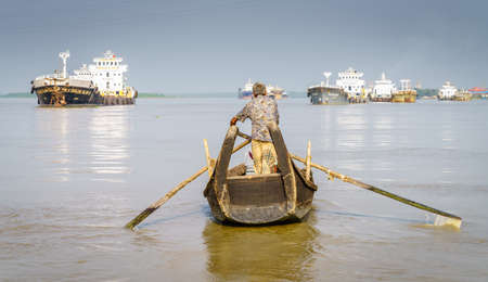 Chittagong, Bangladesh, December 22, 2017: Man is rowing a boat on the Karnaphuli River in Chittagong with fishing ships in the backgroundのeditorial素材