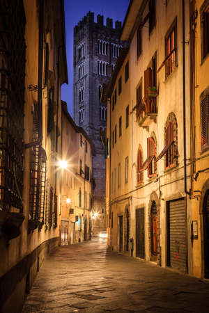 A street in the historic part of Lucca, Italy at night with a view of the Lucca Cathedral towerの写真素材