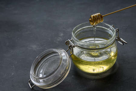 Glass jar full of honey with metal honey dipper on dark rustic backgroundの写真素材