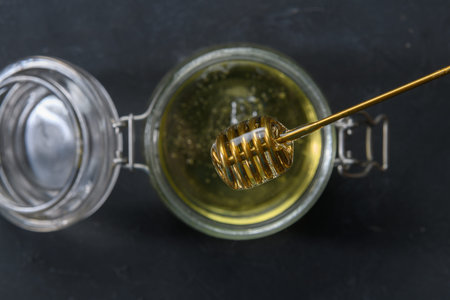 Glass jar full of honey with metal honey dipper on dark rustic background