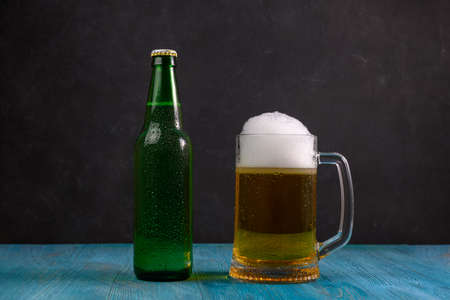Mug of beer and green bottle with beer on wooden table on dark backgroundの写真素材