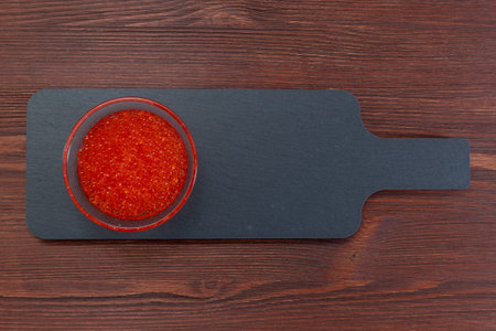 Red caviar in the glass jar on the dark brown wooden backgroundの写真素材
