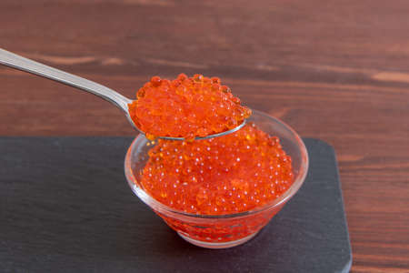 Red caviar in glass jar with silver spoon on the dark brown wooden backgroundの写真素材