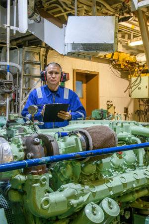 Marine Engineer in blue overall working in Engine room of ship. Work at sea. Motorman.
