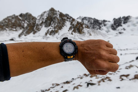 Man's hand with electronic watch showing altitude with snowy mountains on background. Climbing and hiking concept.の写真素材