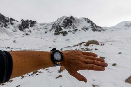 Man's hand with electronic watch showing altitude with snowy mountains on background. Climbing and hiking concept.の写真素材