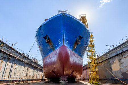 Cargo vessel in dry dock on ship repairing yard. Bulbous bow.