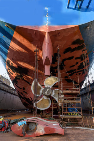 Cargo vessel in dry dock on ship repairing yard. Variable pitch propeller and rudder. Welder working on ship repairing yard.の写真素材