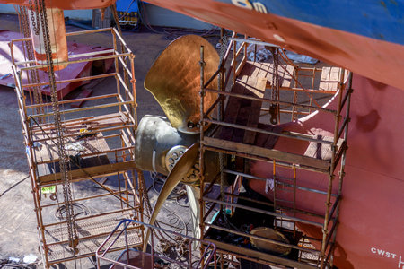 Cargo vessel in dry dock on ship repairing yard. Variable pitch propeller and rudder. Welder working...