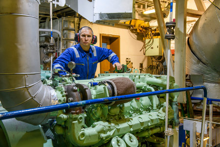 Marine Engineer in blue overall working in Engine room of ship. Work at sea. Motorman.