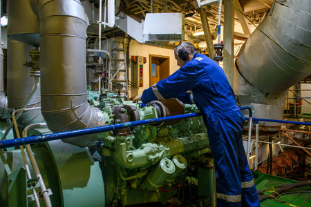 Engine room operations aboard a vessel. Work in the ship's engine room showing maintenance of marine...