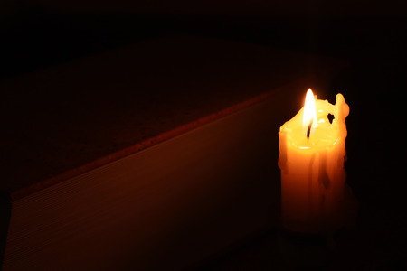 Burning candle near the big book in the darkの写真素材