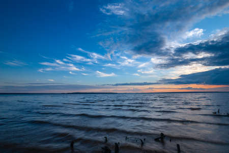 Blue tranquil minimalist landscape with lake with wavy water surface with horizon under dramatic cloudy sky, simple beautiful calm natural blue backgroundの写真素材