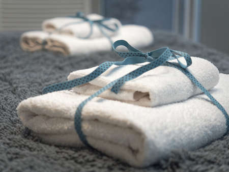 Small white towels folded in half bandaged with a ribbon lie on the bed.の写真素材