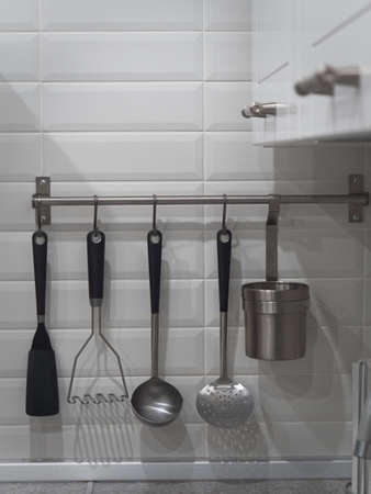 Ladles and other appliances for cooking hang on the wall of a light kitchen.の写真素材