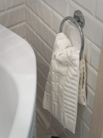 A small cream-colored hand towel hangs on a chrome metallic ring in the bathroom.の写真素材