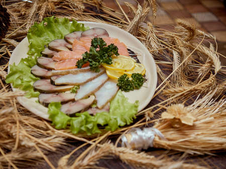 Pieces of smoked fish of different varieties are laid out on a plate decorated with green salad leaves.の写真素材