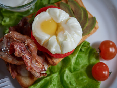 Poached egg cooked and served for breakfast along with roasted meat and fresh tomatoes.