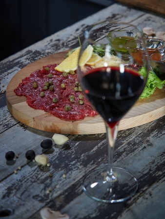 A large piece of raw beef meat is served on a table on a wooden tray with sauces for meat.の写真素材