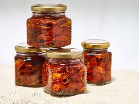 Home-made canned red dried cherry tomatoes are packed in small glass jars.の写真素材