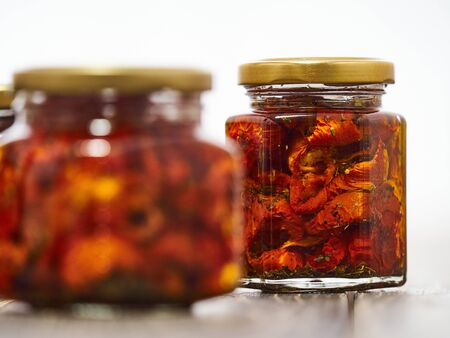 Home-made canned red dried cherry tomatoes are packed in small glass jars.の写真素材