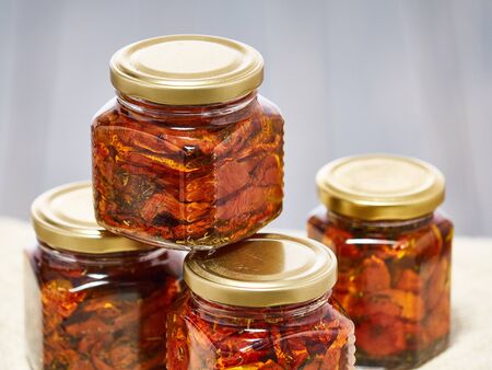 Home-made canned red dried cherry tomatoes are packed in small glass jars.の写真素材