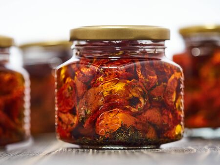 Home-made canned red dried cherry tomatoes are packed in small glass jars.の写真素材