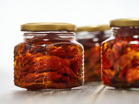 Home-made canned red dried cherry tomatoes are packed in small glass jars.の写真素材