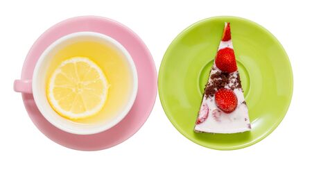 lemon tea with a whole slice of lemon in a pink cup, next to a piece of strawberry cake on a green saucer, close-up on a white backgroundの写真素材